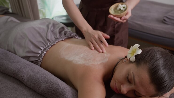 Hænderne på en spa-salon specialist smører lotion på ryggen af en kvindelig klient