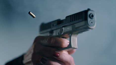 persona con esmalte de uñas rojo disparando una pistola y expulsando el casco