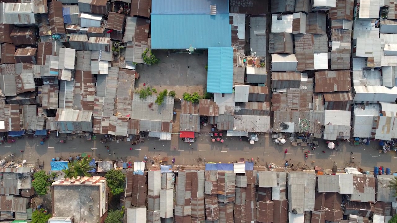 Drohnenaufnahme eines Slums in der Stadt Dhaka, eine Straße mitten im Slum und sich bewegende Menschen.