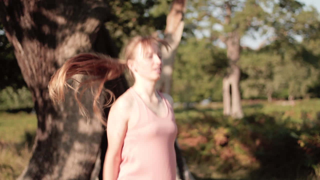 화창한 날 탁 트인 녹색 정원에서 한 여성이 나무 앞에서 점핑 잭을 하고 있습니다.