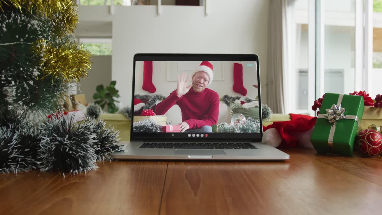 hombre afroamericano albino sonriente con sombrero de papá noel en una videollamada en una computadora portátil