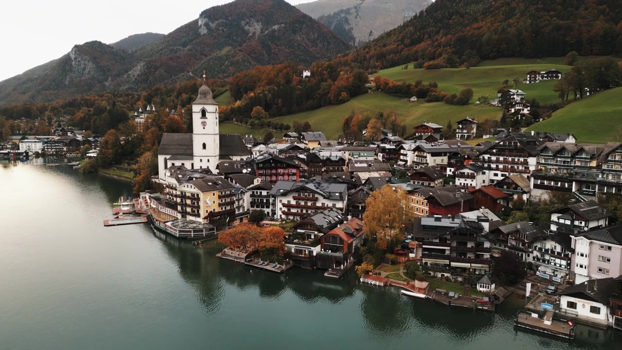 Bevægeligt luftfoto med drone af Wolfgang am Wolfgangsee langvejsfra på en regnvejrsdag.