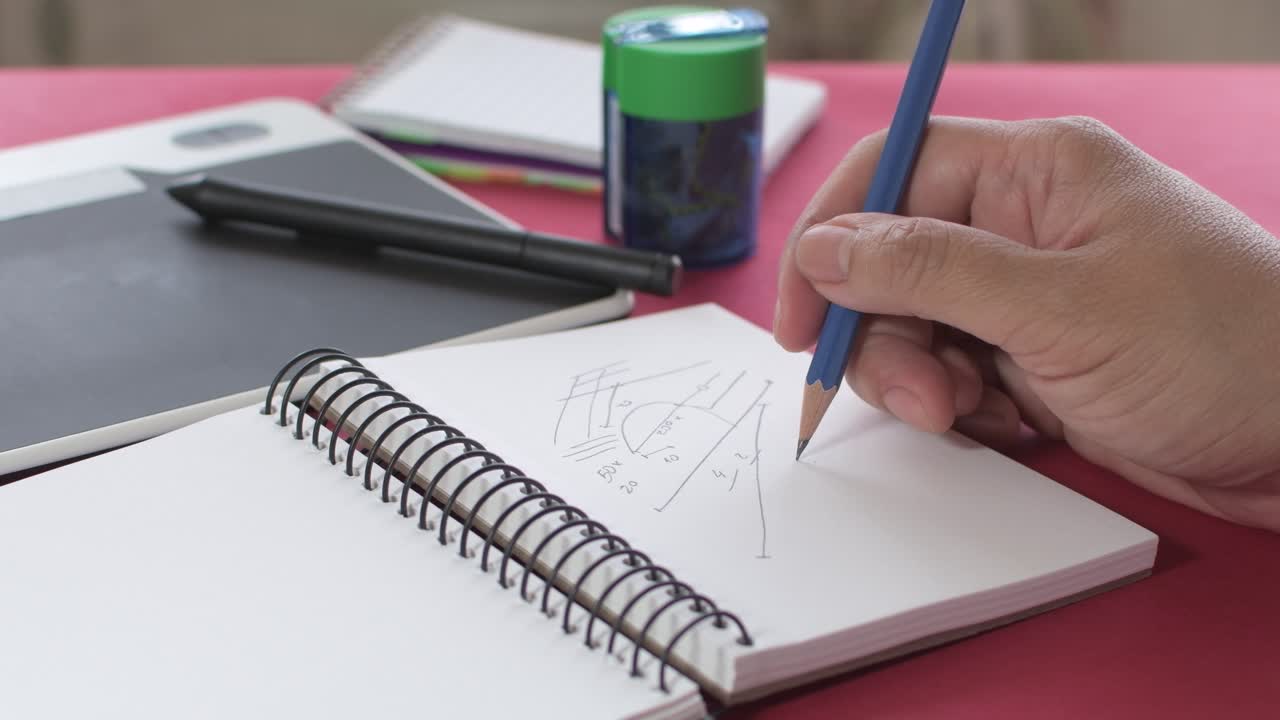 Woman's hands taking notes with a pencil in a notebook, together with a pencil sharpener and graphic tablet in the background.