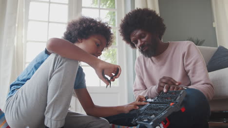 Mixed-race-pre-teen-boy-sitting-on-the-floor-with-his-father,-using-pliers-to-assemble-a-kit-toy,-low-angle