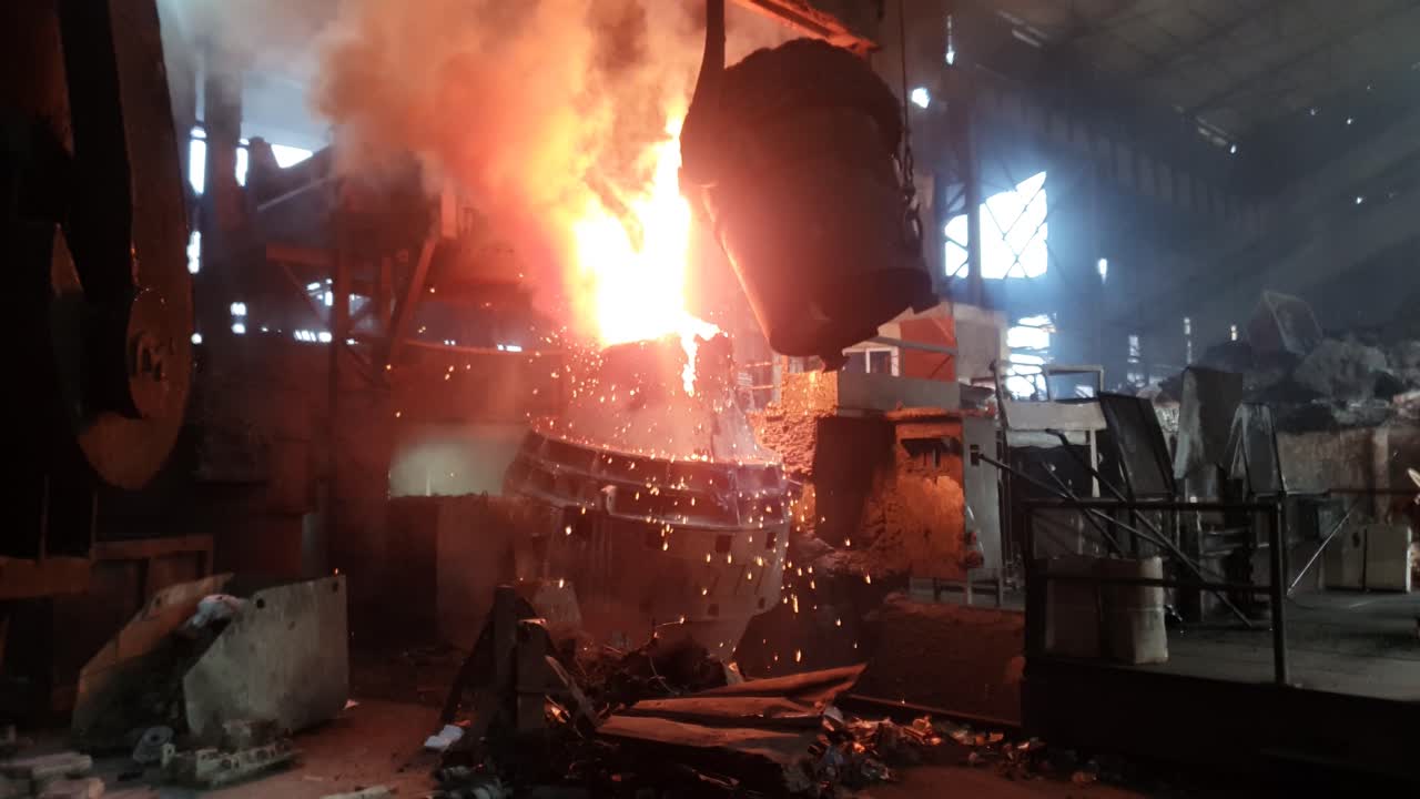 Hot liquid molten metal being poured from ladle into casting flask at steel fabrication industry