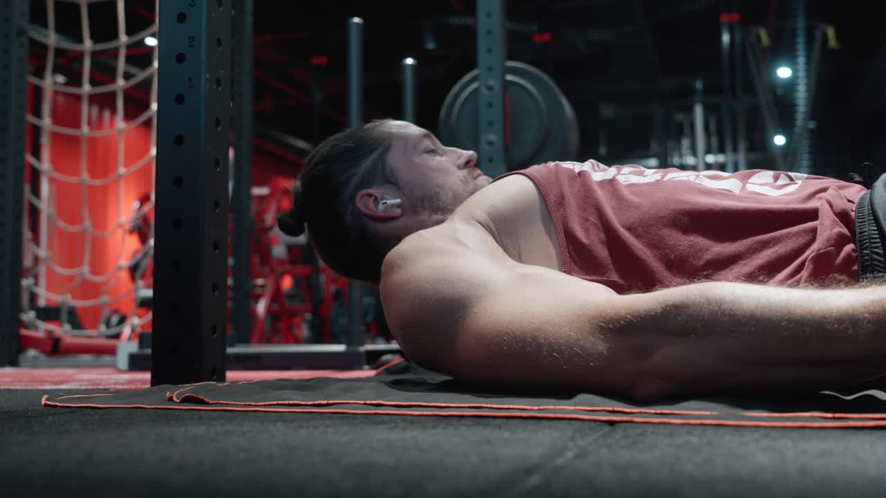 still shot of a handsome young Caucasian man doing sit-ups on a mat in a black and red gym