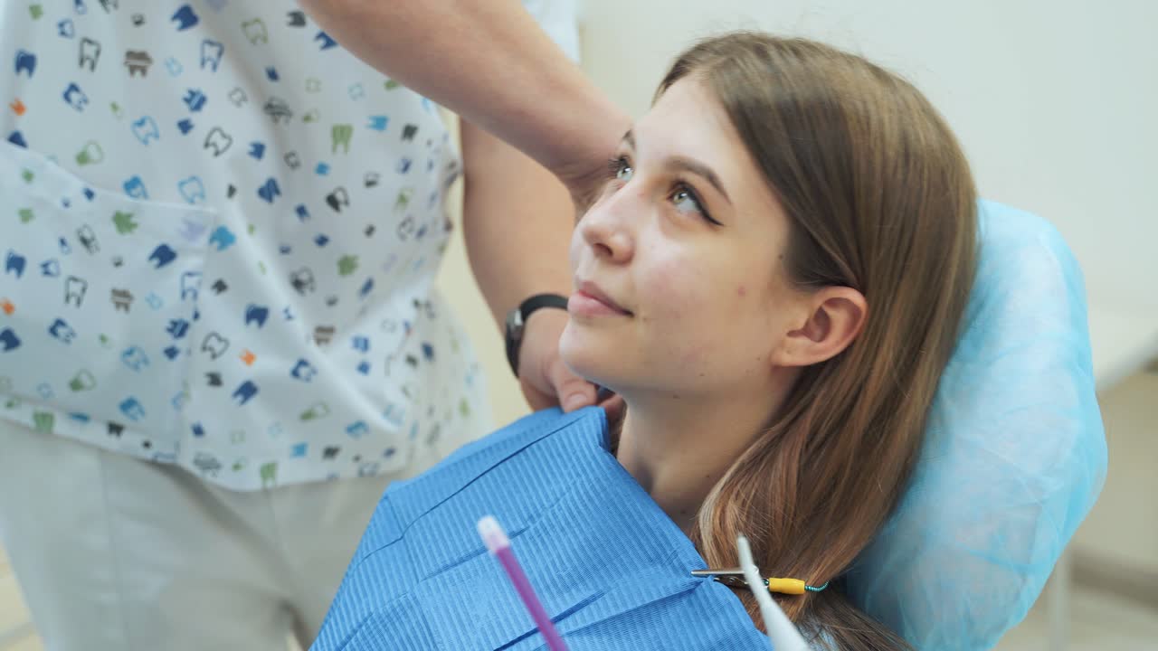 Il dentista mette un bavaglino dentale a una bambina seduta su una poltrona. Clinica dentale.