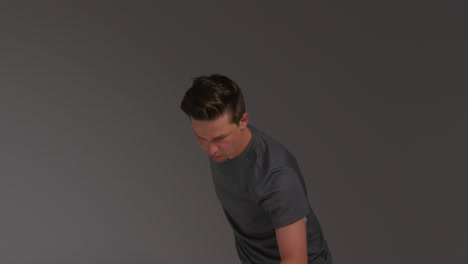 studio shot of male tennis player serving in match hitting ball with racket against grey background