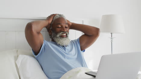 Senior-man-having-a-video-chat-on-his-laptop-in-bed-at-home