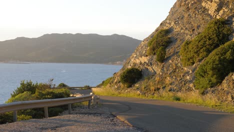 Zeitlupenaufnahme-Der-Nachmittagssonne-Auf-Kurviger-Asphaltstraße-An-Der-Küste-Mit-Klippen-In-Chia,-Südsardinien,-Italien