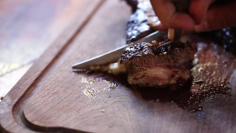 Close-up-view-of-Male-hand-with-a-knife-slicing-a-piece-of-meat-on-cutting-Board