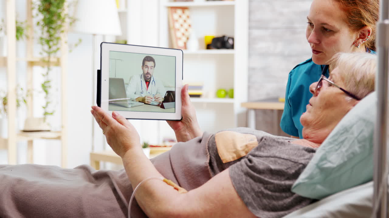 Mujer mayor con discapacidad acostada en cama de hospital haciendo una videollamada en línea con un médico