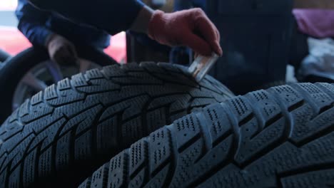 primer plano de un hombre comprobando la banda de rodadura de un neumático de automóvil con un calibre