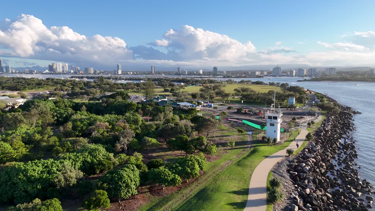 Drone captures scenic Gold Coast landscape with lush greenery, waterway, and skyline during sunset. Vibrant colors and serene atmosphere