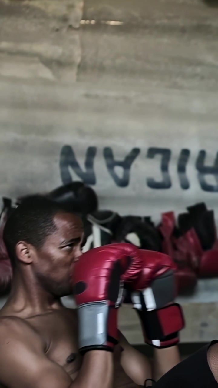 Video verticale: Un pugile adulto guarda un sacco da boxe, alza i guantoni e lo colpisce per migliorare la forma fisica.
