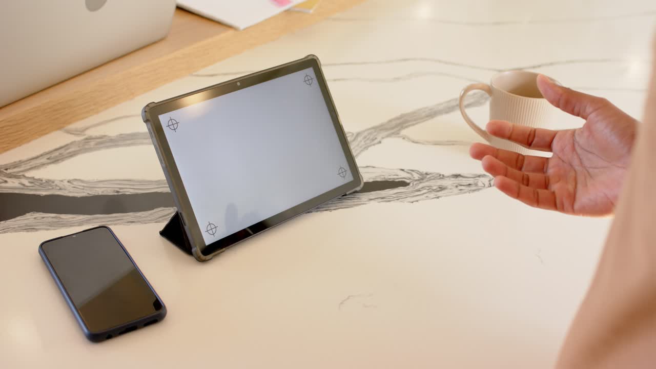 Coffee mug entering frame as woman's hand positioning it on tablet screen over desk for demo