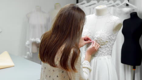 Portrait-of-a-girl-creating-a-wedding-dress-by-exclusive-order-sewing-fabrics-and-rhinestones-on-a-dress-dressed-in-a-mannequin.-production-of-wedding-dresses.-Little-business