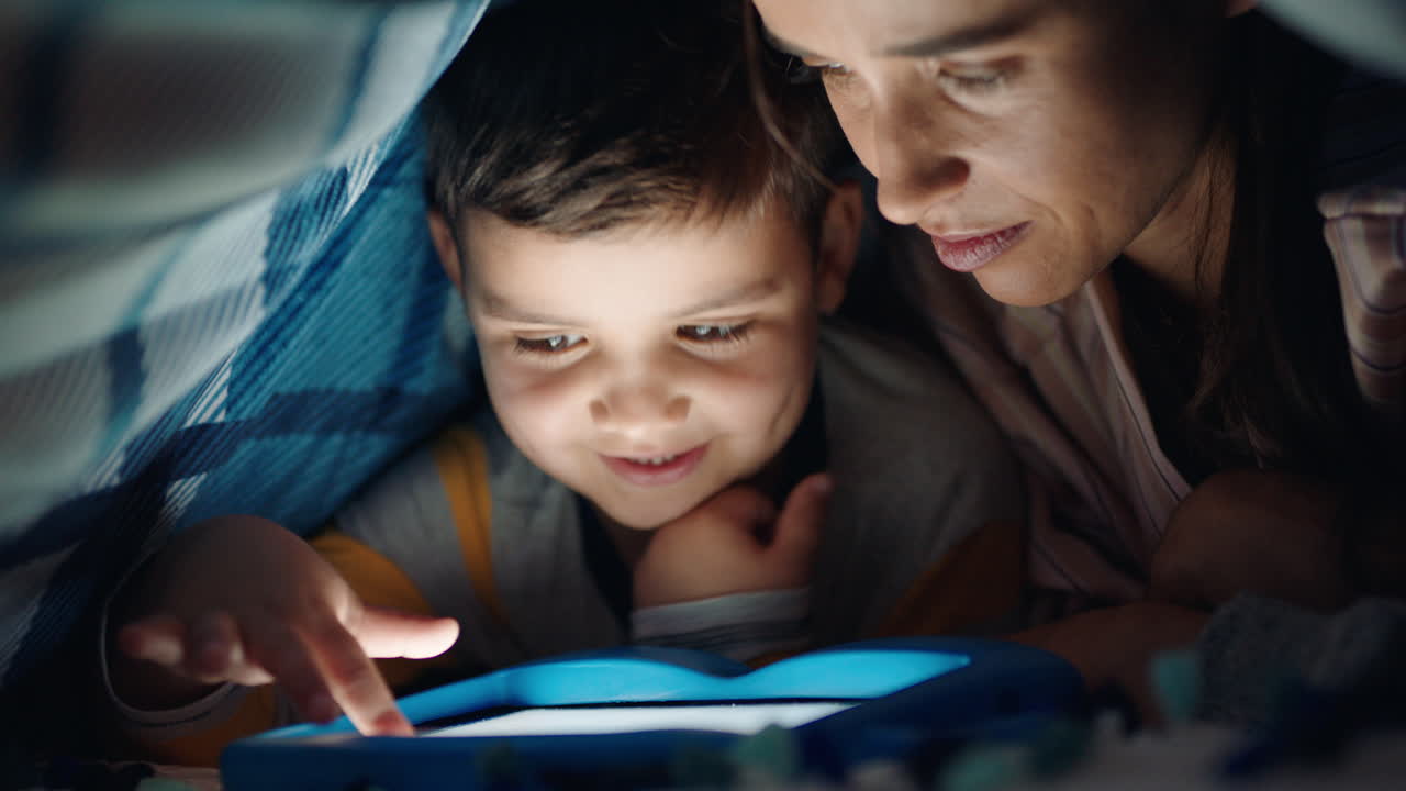 madre e figlio che usano un tablet computer sotto la coperta che giocano a giochi sulla tecnologia touchscreen il bambino che si diverte prima di andare a letto