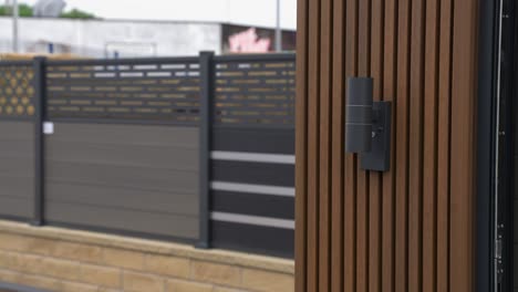 an up and down light sitting on the end of brown luxury cladded garden room in a garden showroom with different examples of fencing in the background