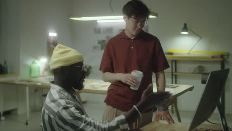 Two diverse male coworkers discussing a project at a computer in a creative office space