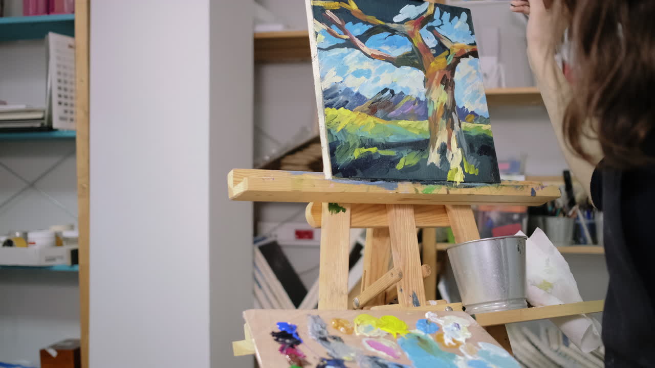 artista pintando un paisaje de un árbol con montañas en un estudio de arte