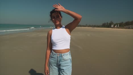 A-beautiful-young-woman-covers-her-face-from-the-sunlight-with-her-hand-in-a-white-top-on-a-breach