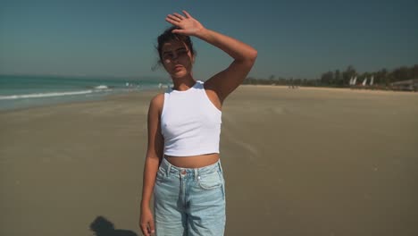 a beautiful young woman covers her face from the sunlight with her hand in a white top on a breach