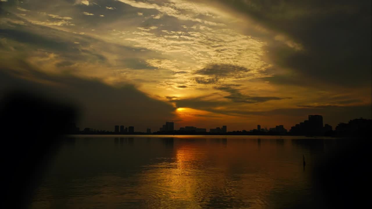 Timelapse view of sunset over Han River with dramatic clouds glowing sky and city skyline reflecting on calm water in Da Nang Vietnam