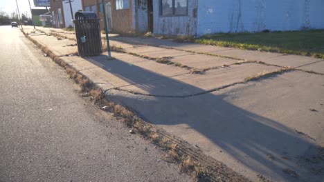 orbiting shot of dirty city curb in detroit with overgrown weeds and debris with long shadows during the evening