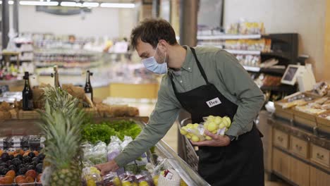 Male-assistant-in-supermarket-food-store-worker-in-medical-mask-and-apron-arranges-packed-products-on-shelves