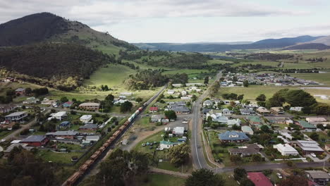 drone shot of train passing through rural green country town in tasmania, australia