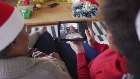 madre y hija afroamericanas usando una tableta para una videollamada de navidad con una mujer en la pantalla