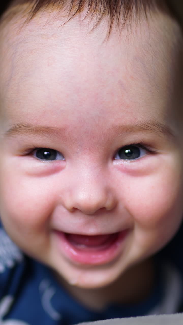 Nice smiley face of a newborn baby. Close up portrait of a little kid smiling cheerfully to the camera. Dark backdrop in blur. Vertical video