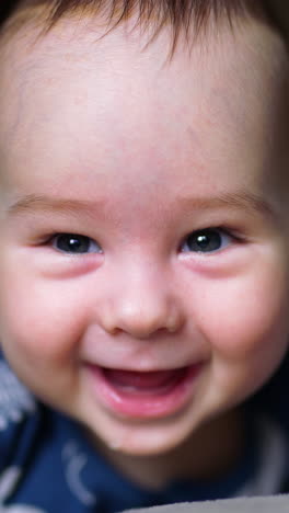 nice smiley face of a newborn baby. close up portrait of a little kid smiling cheerfully to the camera. dark backdrop in blur. vertical video