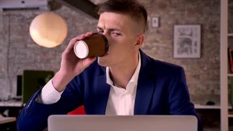 joven hombre de negocios serio está viendo en la computadora portátil, bebiendo café, concepto de comunicación, concepto de negocio