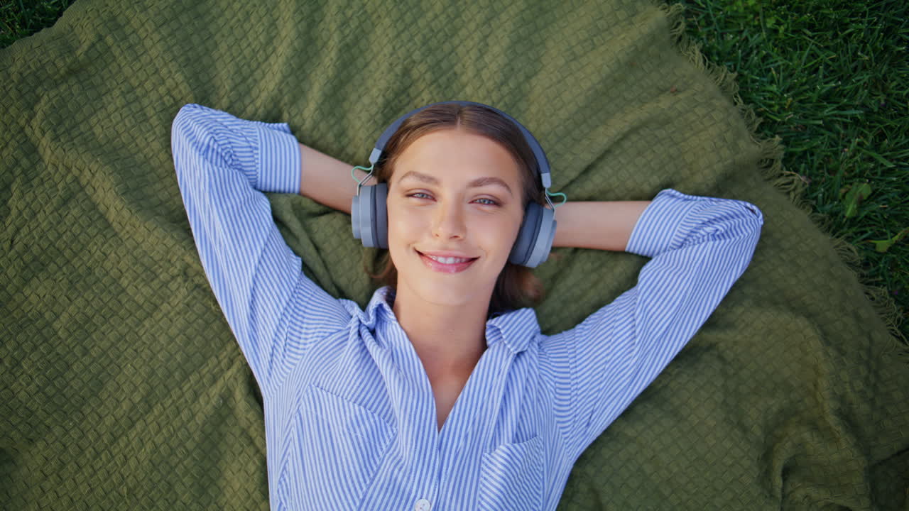 Woman listening music nature lying picnic blanket in headphones closeup