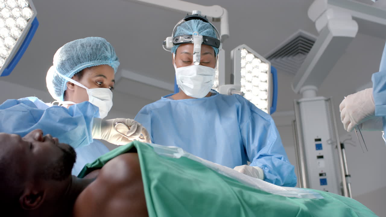 Chirurghe di diverse etnie che operano un paziente afroamericano in sala operatoria, al rallentatore.