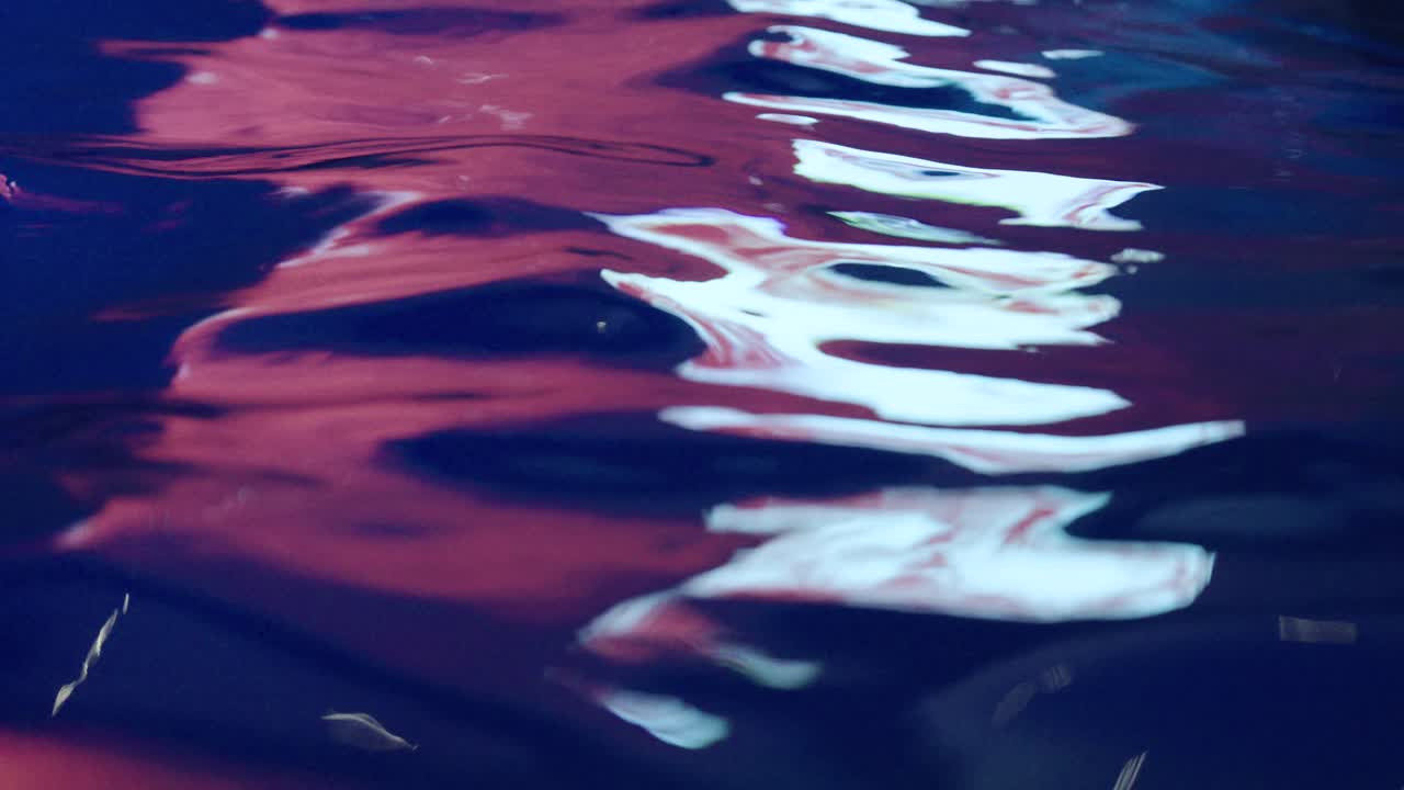 A close-up of water with soft waves and vivid reflections in blue, red, and white—capturing a dynamic and artistic moment on the surface