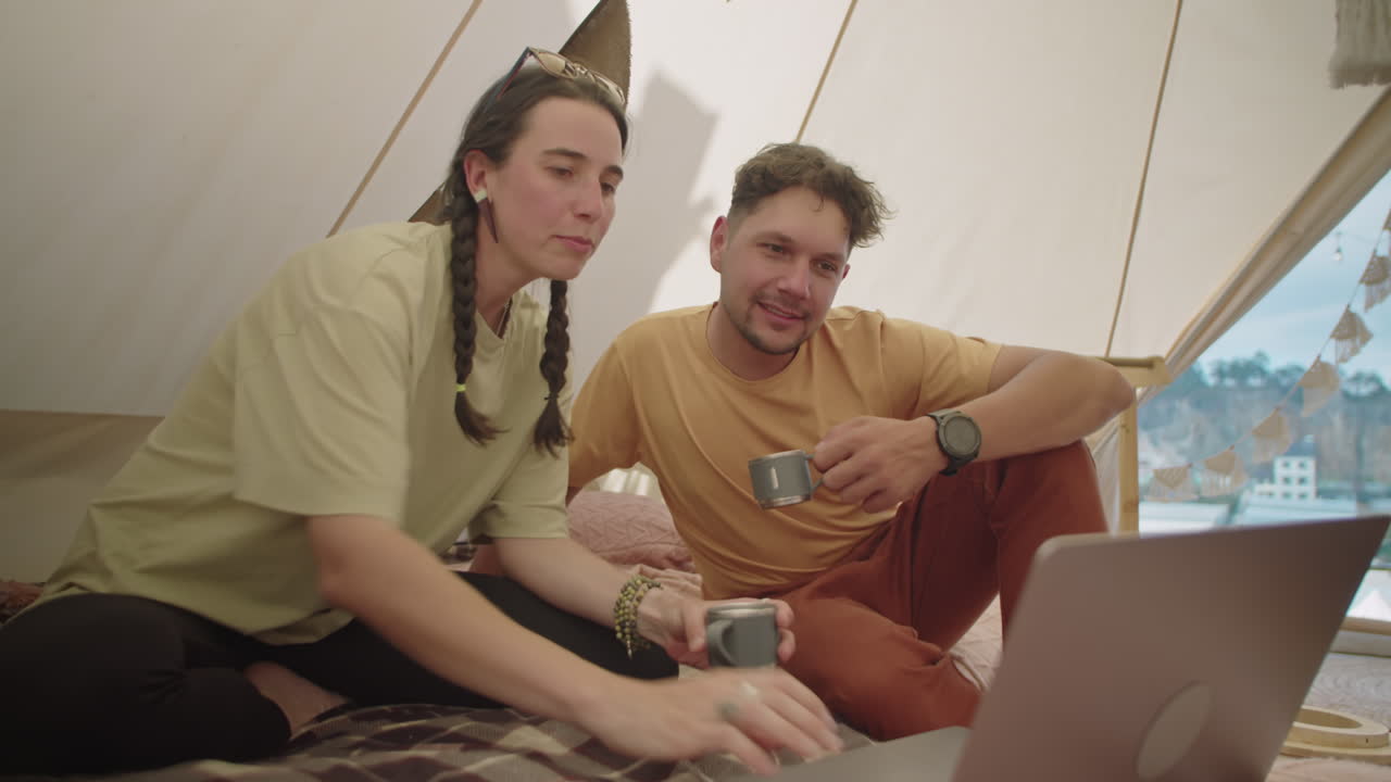 Coppia che beve il tè, parla e utilizza un laptop in una tenda glamping