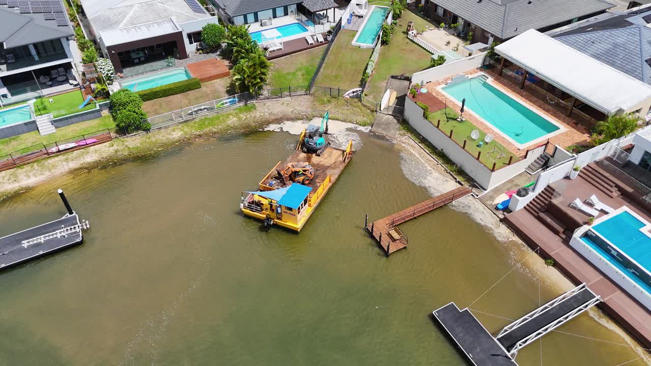 드론 영상은 수영장과 함께 럭셔리 주택 근처의 운하에서 일하는 배와 크레인을 포착합니다.
