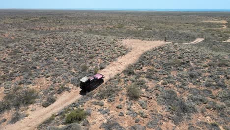 toma aérea de un vehículo safari 4x4 conduciendo en un desierto montañoso durante la luz del sol, una persona caminando