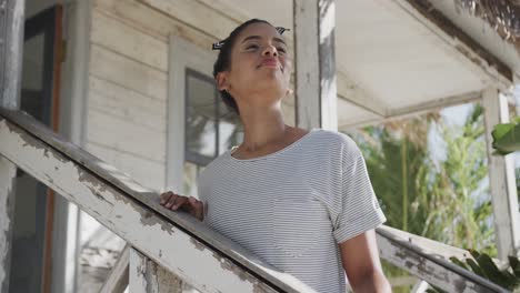 feliz mujer biracial de pie en los escalones de la casa de playa de madera sonriendo, en cámara lenta