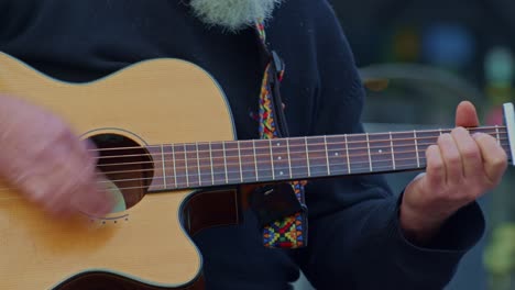 guitarist plays on wooden acoustic guitar, closeup view of hands, fingers, frets and strings