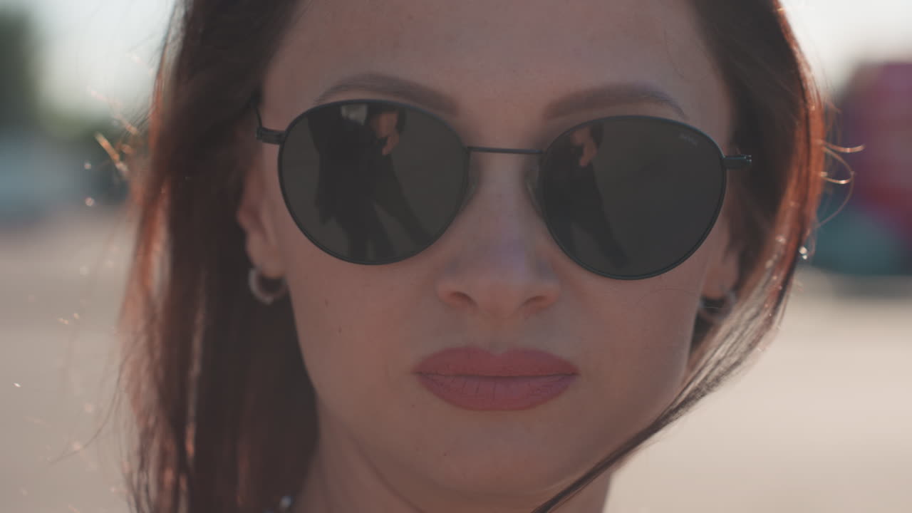 Close up of woman putting on sunglasses near face preparing to wear them outdoors, sunlight reflecting on skin and glasses frame, showcasing beauty and elegance