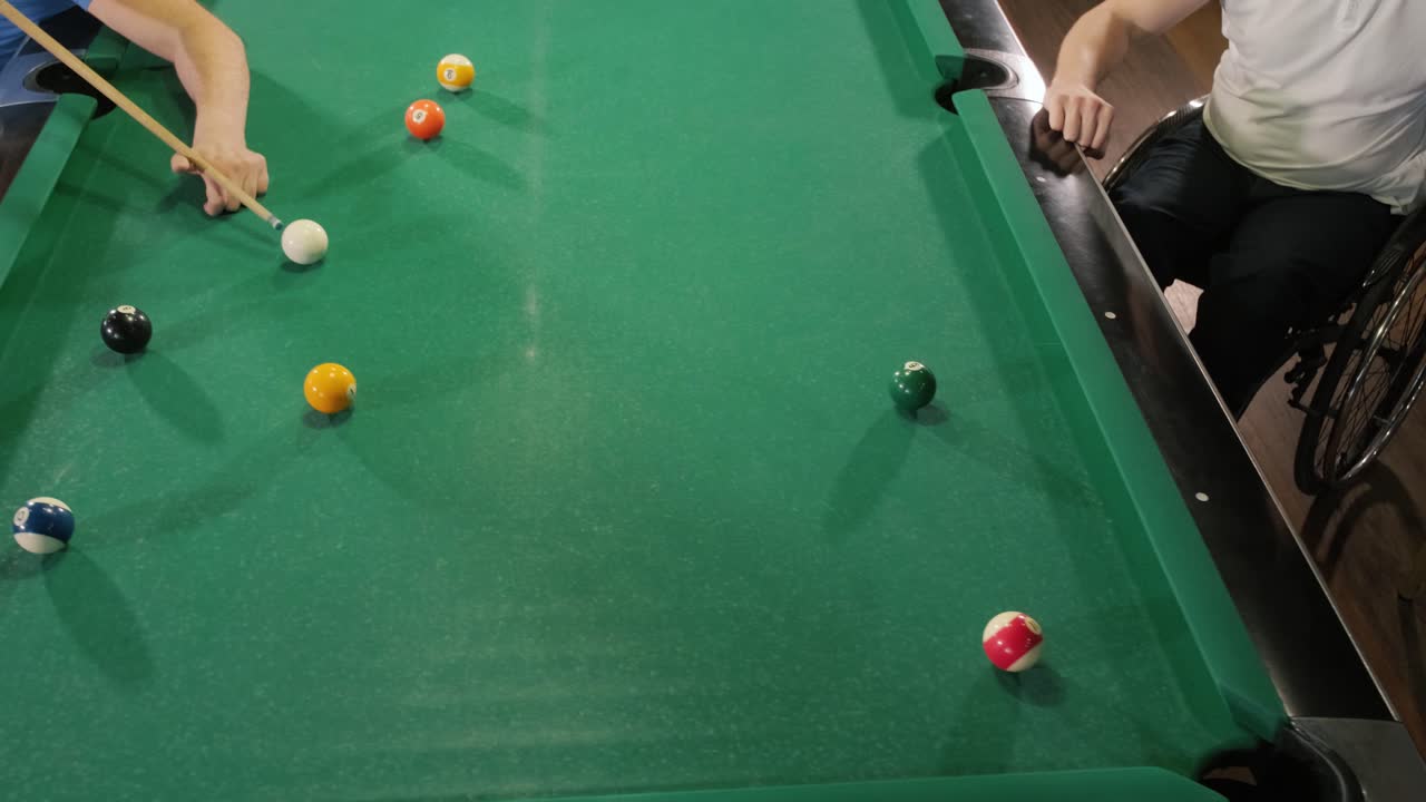 Adult men with disabilities in a wheelchair play billiards in the club