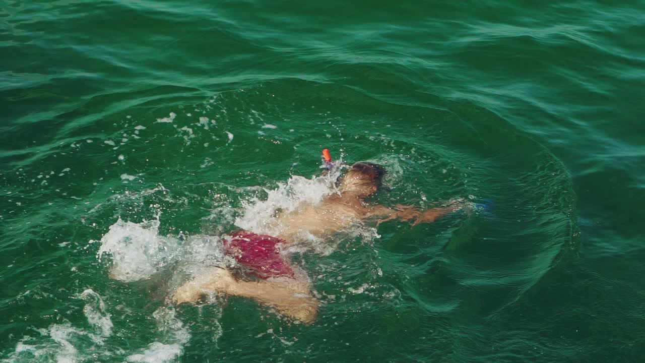 adult man in red shorts is swimming under water in a mask and with snorkel in the sea in the summer. Slow motion