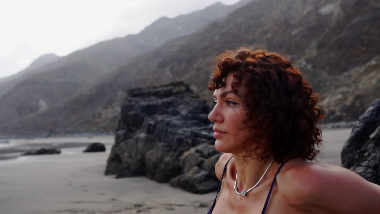 In a graceful display, a young and slim female athlete practices push-ups on a rock by the ocean in slow motion