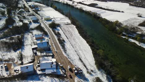 Aerial-view-of-a-van-driving-in-a-rural-landscape-covered-with-snow-next-to-Cetina-river-on-a-beautiful-winter-day,-Dalmatian,-Croatia