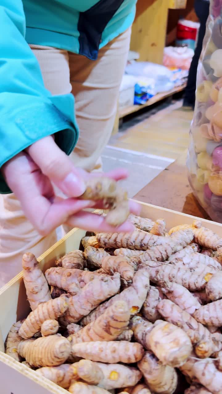 Donna che sceglie radice di curcuma fresca in una bancarella del mercato