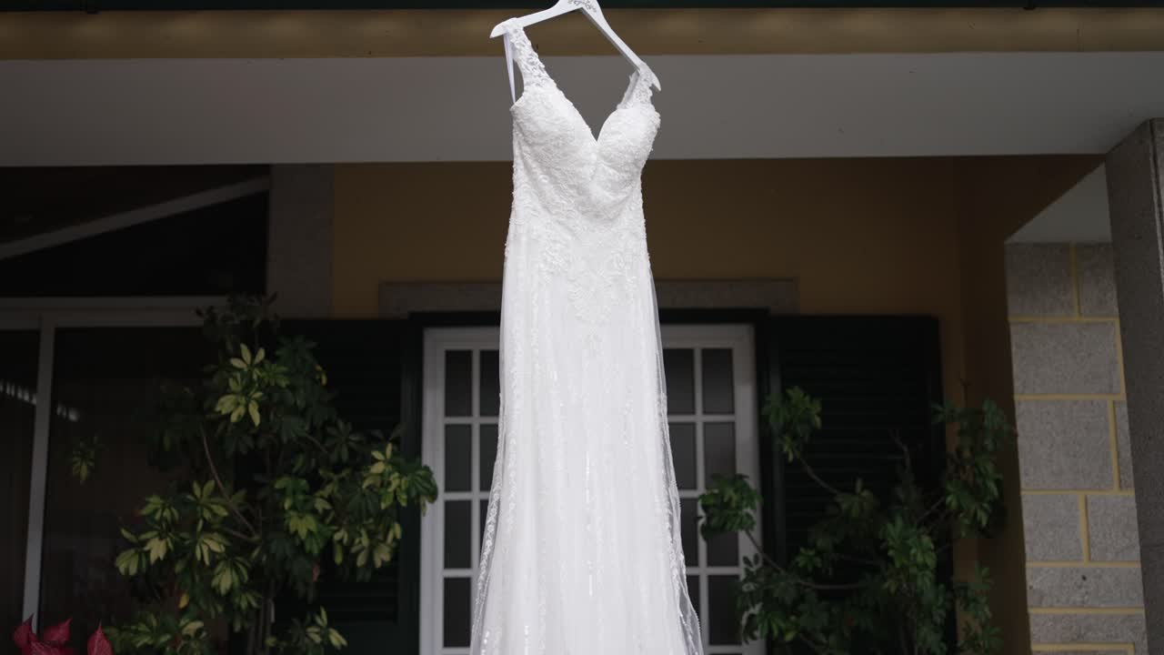 elegant white bridal gown hanging outdoors in front of a house window and greenery